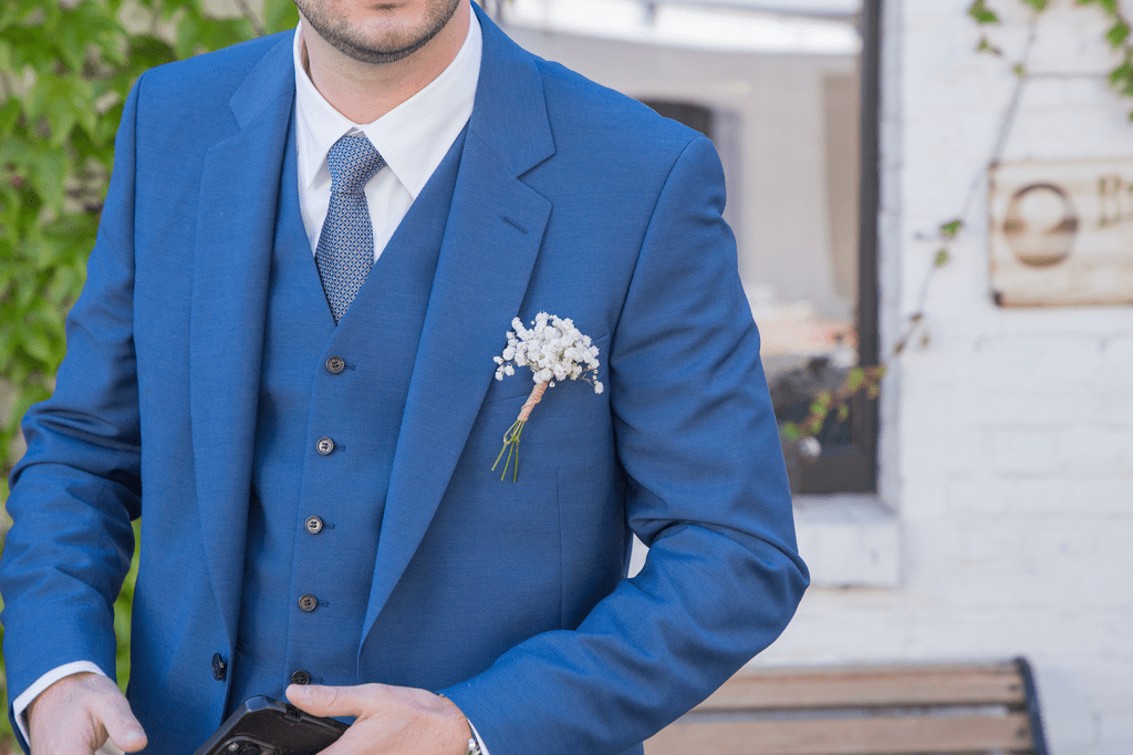 Photo d'un costume bleu de marié avec une cravate bleue et un petit bouquet de fleurs
mur blanc en arrière plan