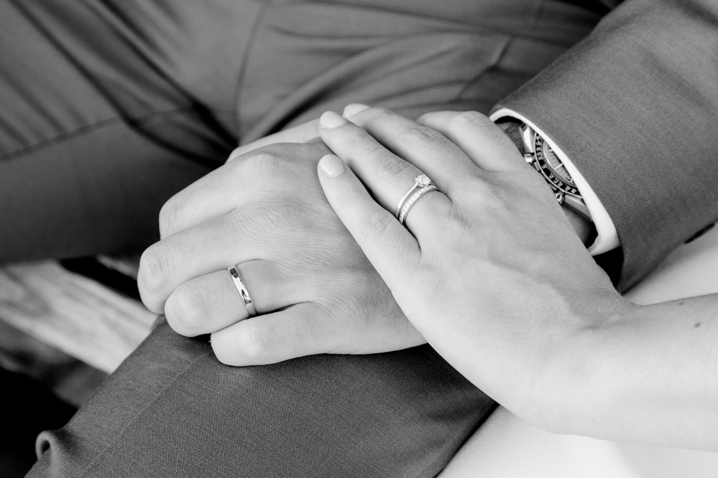 photo en noir et blanc des mains des mariés, posées sur une jambe. Alliances mie en évidence