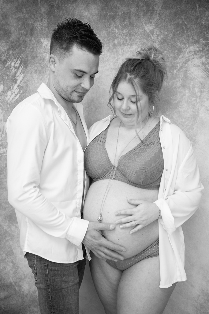 photo de grossesse noir et blanc, les parents regardent et caressent le ventre de la maman