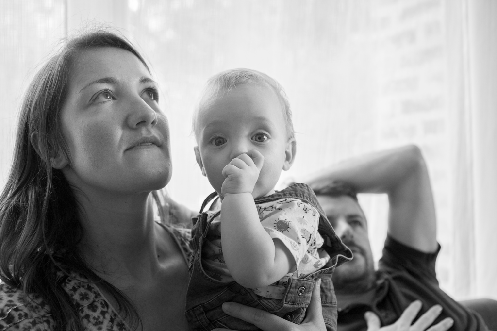 photo en noir et blanc de deux parents avec leur bébé suçant son pouce 