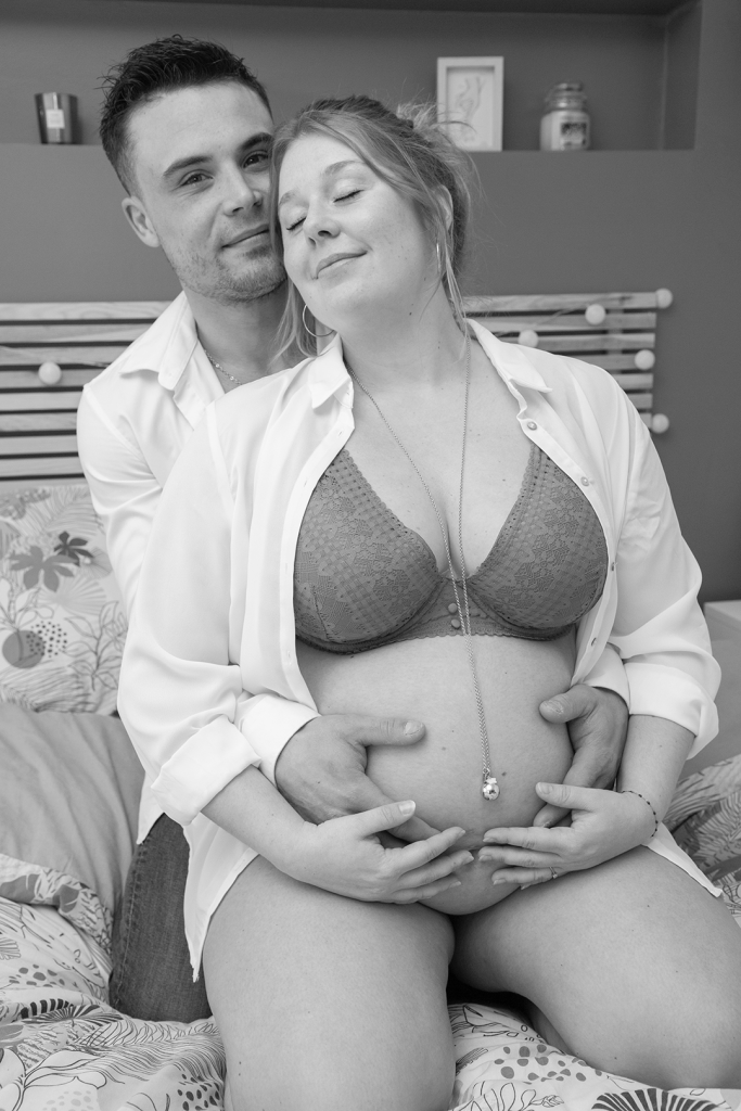Photo de grossesse noir et blanc, le père tient le ventre de la maman sur le lit