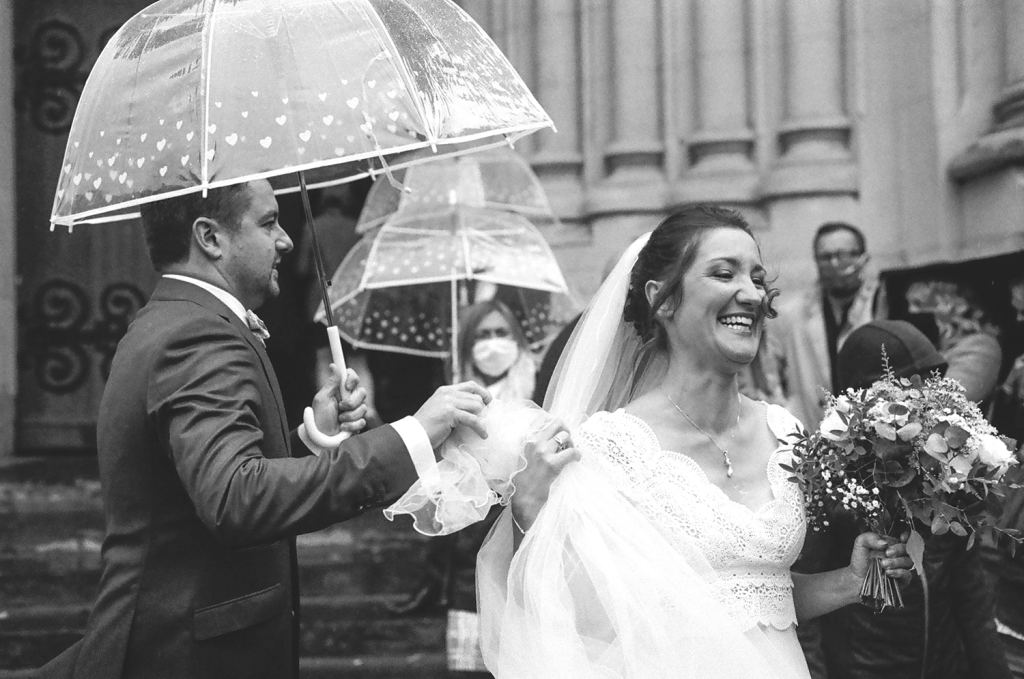 photo de la mariée souriante sortant de l'église, son mari l'accompagne noir et blanc