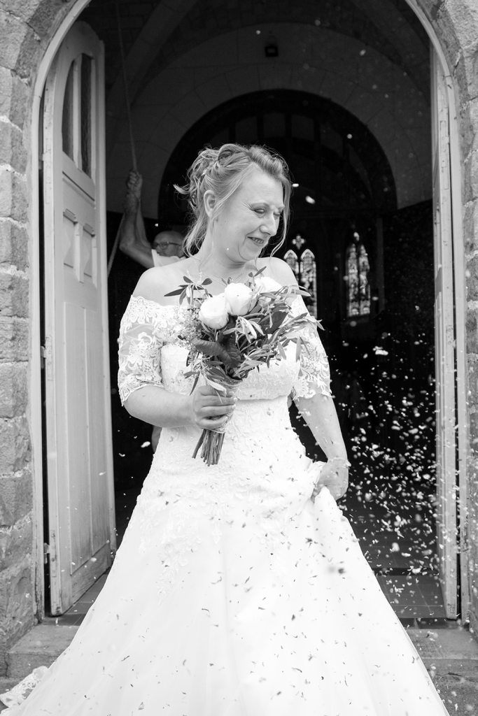 photo mariée sortie de l'église noir et blanc avec des confettis et bouquet de fleurs