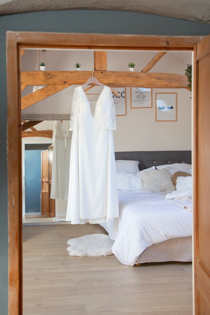 photo dans une chambre de robe de mariée accrochée à une poutre. 
on y voit un lit et des cadres accorchés au mur